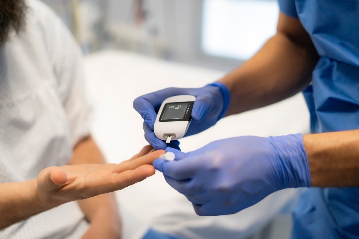 Doctor is using glucometer for measuring blood glucose level of patient in hospital room