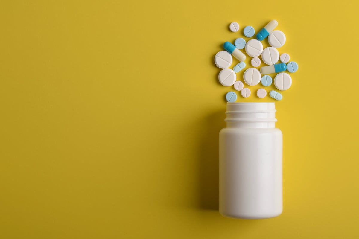 Various pills spilling from a medicine bottle on a yellow background, top view, with copy space for text. Medical concept.